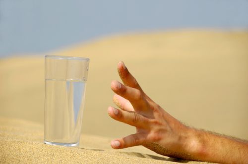 Hand is reaching for a fresh glass of cold water in desert.