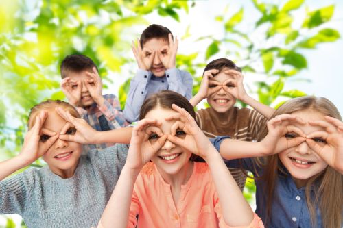 childhood, summer, friendship and people concept – happy children making faces and having fun over green natural background