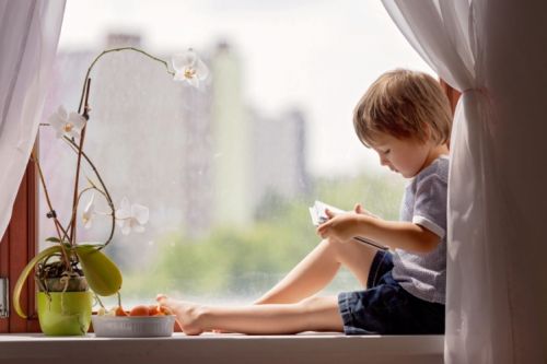 Cute little boy, sitting on the window, playin on tablet