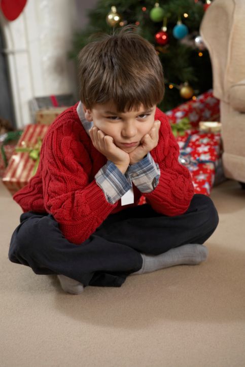 Boy (6-8) sitting on floor sulking, Christmas tree in background