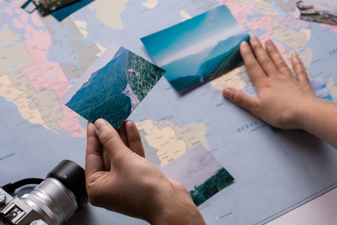 Close-up of unrecognizable tourist watching photographs of travel and putting it on paper map