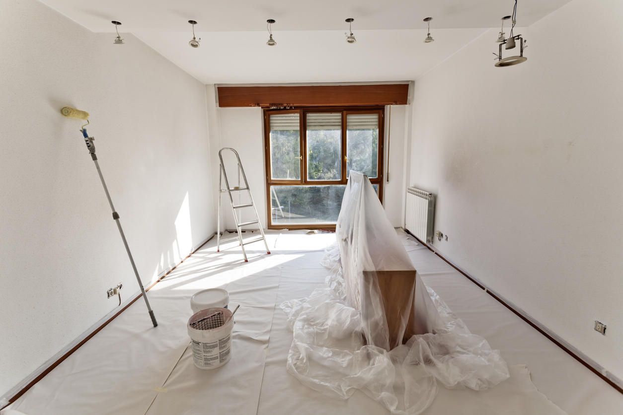 A room is being prepped for painting with drop cloths, a paint roller, and a ladder.